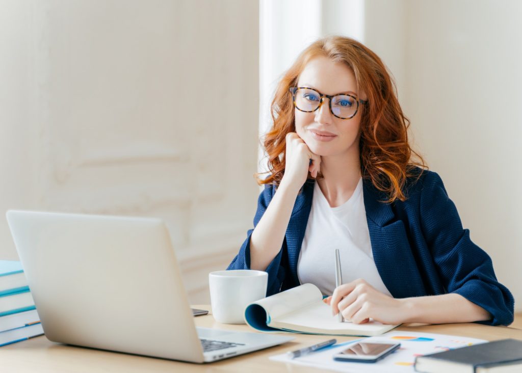 Redhead curly woman office worker analyzes data, makes accounting report, poses in coworking office